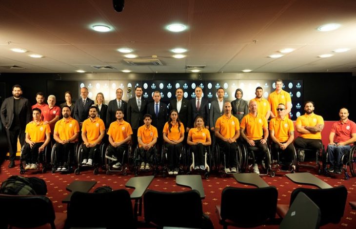 Fuzul Tasarruf Finansman A.Ş. ile Galatasaray yöneticileri ayakta duruyor, Tekerlekli Sandalye Basketbol Takımı sporcuları önlerinde bulunuyor.