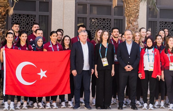 Gençlik ve Spor Bakanı Osman Aşkın Bak ve TBMM Engelli Bireylerin Sorunlarını Araştırma Komisyonu Başkanı Mehmet Muharrem Kasapoğlu, önde yer alıyor. Arkalarında ise Suudi Arabistan'daki 6. İslami Dayanışma Oyunları'na katılan milli sporcular ve Türk bayrağı yer alıyor.