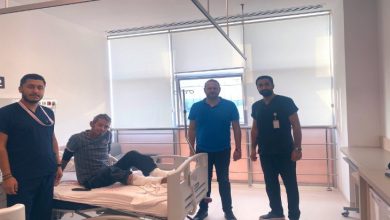 Aydınlık bir hastane odasında dört kişi görülüyor. Ortada, hastane yatağında oturan bir hasta var; ayakları bandajlı. Yanında üç sağlık çalışanı ya da görevli ayakta duruyor. Odanın büyük pencerelerinden gün ışığı süzülüyor, ortam temiz ve sakin bir tedavi alanı hissi veriyor.