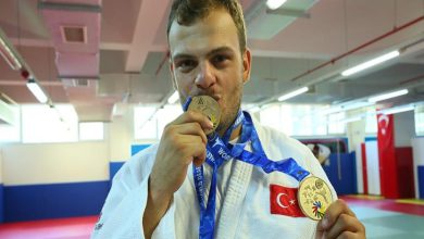 Milli judocu Samet Bulut bir elinde madalya tutup öperek diğer elinde madalya tutarak poz veriyor.