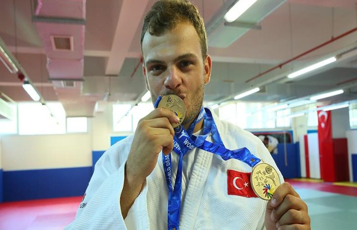 Milli judocu Samet Bulut bir elinde madalya tutup öperek diğer elinde madalya tutarak poz veriyor.