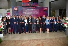 Geniş bir kalabalığın katıldığı resmi bir açılış töreni görülüyor. Uzun bir kurdele boyunca yan yana dizilmiş katılımcılar, makaslarıyla toplu bir kurdele kesimine hazırlanıyor. Arkada büyük bir afiş, bilimsel kongre ve sergi etkinliğinin adını taşıyor. Herkes şık giyimli, ortamda tören havası ve heyecanlı bir kalabalık enerjisi var.