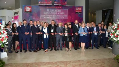 Geniş bir kalabalığın katıldığı resmi bir açılış töreni görülüyor. Uzun bir kurdele boyunca yan yana dizilmiş katılımcılar, makaslarıyla toplu bir kurdele kesimine hazırlanıyor. Arkada büyük bir afiş, bilimsel kongre ve sergi etkinliğinin adını taşıyor. Herkes şık giyimli, ortamda tören havası ve heyecanlı bir kalabalık enerjisi var.