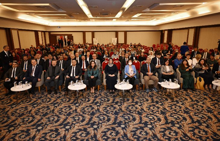 Görselde geniş bir konferans salonunda kalabalık bir katılımcı grubu görülüyor. Ön sırada resmi kıyafetli katılımcılar otururken, arkada salonu dolduran çok sayıda kişi dikkatle etkinliği takip ediyor. Ortam, bir konferans veya ödül törenine ait düzenli ve resmi bir atmosfer yansıtıyor.