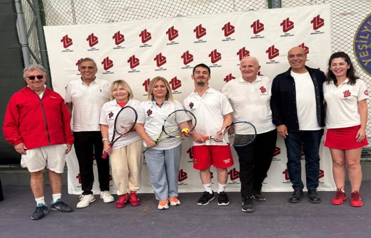 Görselde bir grup kişi tenis kortunda, Türk Böbrek Vakfı logolu fon önünde poz veriyor. Çoğu spor kıyafetleri içinde ve ellerinde tenis raketleri bulunuyor. Arka planda file ve kulüp logosu yer alıyor. Ortam neşeli ve samimi bir turnuva atmosferini yansıtıyor.