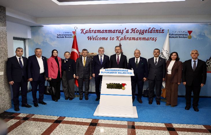 Bir grup yetkili ve görevli, “Kahramanmaraş’a Hoşgeldiniz” yazısının bulunduğu alanda yan yana dizilmiş şekilde poz veriyor. Ortada bir kürsü, arka planda Türk bayrağı ve belediye logosu görülüyor. Herkes resmi kıyafetleriyle kameraya bakıyor.