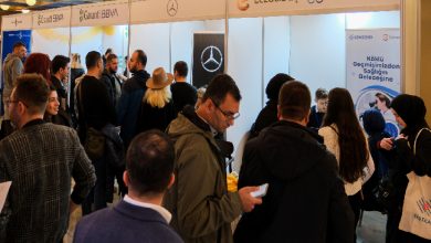 Kalabalık bir grup, Garanti BBVA, Mercedes, Eczacıbaşı ve Gensenta stantlarının yer aldığı bir fuar alanında buluşmuş. Katılımcılar firmalarla görüşüyor, bazıları bilgi alıyor.