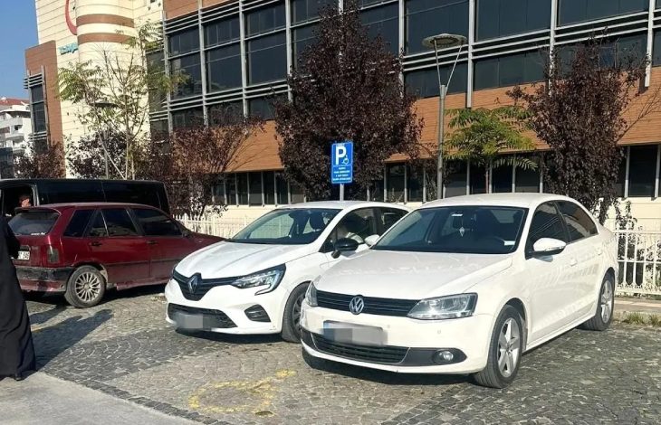 İki beyaz otomobil engelli park alanında bulunuyor.
