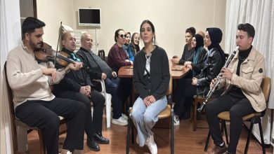 Bir odada sandalyelere oturmuş bir grup görülüyor. Ortada oturan bir kadın kameraya dönük; iki yanda keman ve klarnet çalan müzisyenler var. Arkadaki koro üyeleri dikkatle dinliyor; samimi, üretken ve müzikle dolu bir prova atmosferi hissediliyor.