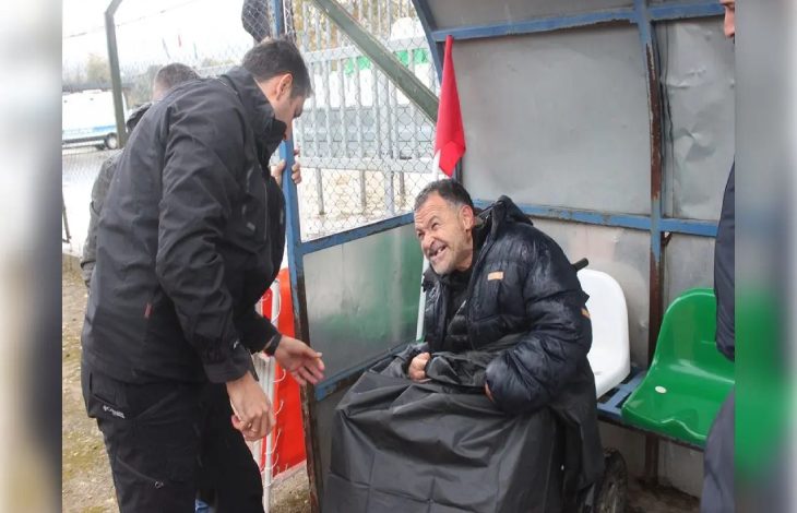 Tekerlekli sandalyesiyle saha kulübesinde bulunan engelli taraftar Nevzat Kahyaoğlu ile yağmurluğunu örten İlçe Emniyet Müdürlüğü Başkomiseri Ramazan Kalkan iletişim kuruyor.