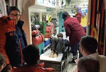 Görselde, bir ambulansın içinde sedyeye yatırılmış bir çocuğa sağlık ekipleri müdahale ediyor. Etrafında ambulans personeli ve görevliler bulunuyor; ortam acil müdahale durumunu yansıtıyor.