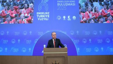 Cumhurbaşkanı Recep Tayyip Erdoğan, büyük bir sahnenin önünde kürsüde konuşma yapıyor, arka planda Dünya Engelliler Günü Buluşması 2025 yazılı mavi bir ekran ve etkinliğe katılan kalabalık bir izleyici grubu görülmektedir.