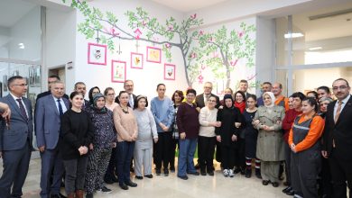 Bir bakım ve rehabilitasyon merkezinde, duvarları ağaç ve kuş figürleriyle süslenmiş aydınlık bir alanda, farklı yaş ve profillerden kalabalık bir grubun yan yana durarak toplu hatıra fotoğrafı çektirdiği görülüyor. Katılımcılar samimi ve resmi karışımı bir ortamda kameraya bakıyor.