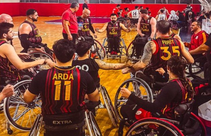 Galatasaray Fuzul Tekerlekli Sandalye Basketbol Takımı oyuncuları maç öncesi sahada halka halinde toplantı yaparken.