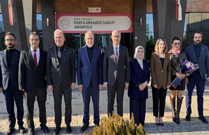 Bir okul binasının önünde yan yana dizilmiş kalabalık bir grup görülüyor. Resmî giyimli katılımcılar kameraya dönük, düzenli bir hat oluşturmuş. Arkada okul tabelası yer alıyor; ortam, anlamlı bir sosyal proje buluşmasının ciddiyetini ve dayanışma havasını yansıtıyor.