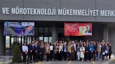 Binanın girişinde geniş bir grup, omuz omuza dizilmiş şekilde toplu fotoğraf veriyor. Üstte “Nöroteknoloji Mükemmeliyet Merkezi” tabelası ve iki büyük kongre afişi görülüyor. Katılımcılar resmi ama enerjik bir duruşla, bilimsel bir etkinliğin açılış anını yansıtıyor.