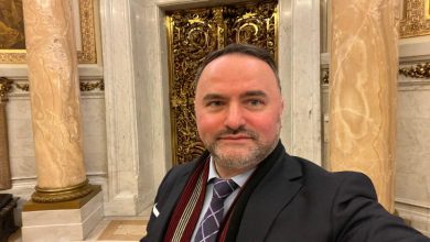 Görselde, takım elbiseli bir erkek tarihi ve görkemli bir iç mekânda selfie çekiyor; arkada mermer sütunlar ve altın işlemeli kapılar görülüyor.