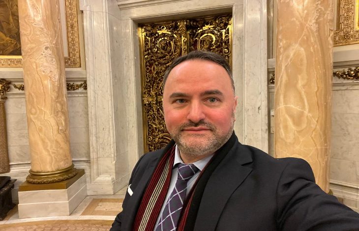 Görselde, takım elbiseli bir erkek tarihi ve görkemli bir iç mekânda selfie çekiyor; arkada mermer sütunlar ve altın işlemeli kapılar görülüyor.