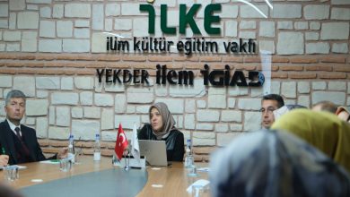 Tuğla görünümlü bir duvar önünde, uzun bir masa etrafında düzenlenen resmi bir toplantı görülüyor. Masada Türk bayrağı, laptop ve su şişeleri yer alırken, konuşmacı kürsüde katılımcılara hitap ediyor; salonda dinleyiciler dikkatle semineri takip ediyor.