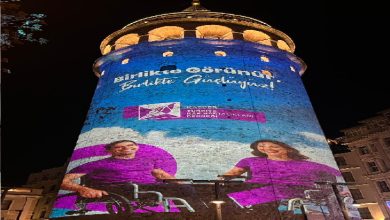 Görselde, Galata Kulesi’nin üzerine yansıtılmış büyük bir farkındalık görseli görülüyor. Işıklı projeksiyon üzerinde mor tonlarında tasarlanmış iki kişi –biri tekerlekli sandalyede– yer alıyor. Üst tarafta “Birlikte Görünür, Birlikte Güçlüyüz!” mesajı öne çıkıyor. Alt kısımda ilgili derneğin logosu bulunuyor. Gece çekilmiş renkli ve etkileyici bir projeksiyon çalışmasıdır.