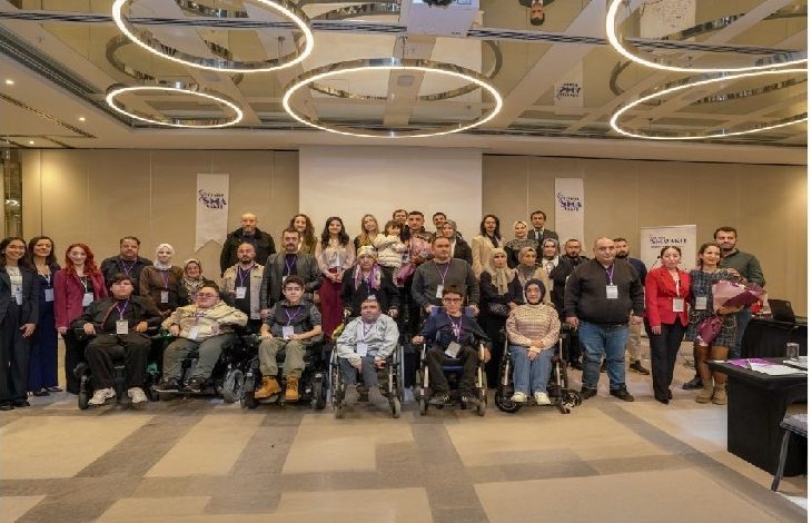 Bir konferans salonunda, Türkiye SMA Vakfı’nın düzenlediği seminer sonrası uzmanlar, aileler ve tekerlekli sandalye kullanan katılımcıların birlikte toplu fotoğraf çektirdiği görülüyor.