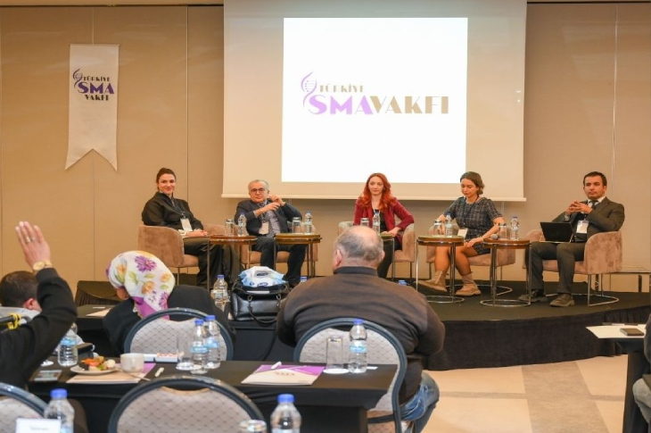 Bir konferans salonunda, Türkiye SMA Vakfı logosu önünde panel masasında oturan konuşmacıların, katılımcıların sorularını yanıtladığı bilgilendirici bir oturum görülüyor.