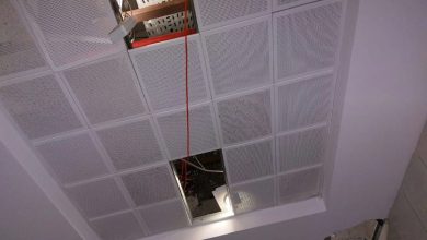 Fotoğrafta, tavanı oluşturan kare formlu, delikli panellerden biri yerinden çıkmış ve tavandaki kablolar ile yapı elemanları açık şekilde görülüyor; ayrıca bir aydınlatma armatürü de boşluktan aşağı doğru ışık veriyor.