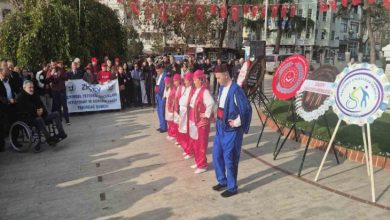 Özel eğitim öğrencileri çelenk bırakılan alanda halk oyunu oynuyor ve engelli dernek üyeleri oyunu izliyor.