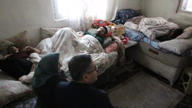 Küçük ve sade bir odada yan yana dizilmiş yataklarda uzanan birkaç kişi görülüyor. Gün ışığı perde aralığından süzülürken, odanın içinde sessiz bir yaşam mücadelesi hissediliyor; başucunda çocuk oyuncakları, ayakta ise onları izleyen yetişkinler.