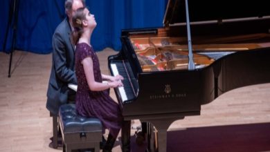 Sahne ışıkları altında bir kadın piyanist, Steinway kuyruklu piyano başında çalıyor; yanında ona eşlik eden başka bir müzisyen oturuyor. Başını hafifçe yukarı kaldırmış, sanki notaları değil, havayı dinliyor.