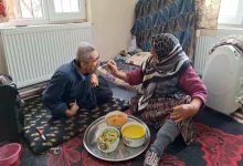 Yerde oturdukları sade bir odada, yaşlı anne tepsideki yemekten kaşıkla karşısındaki engelli oğluna şefkatle yemek yedirirken görülüyor.