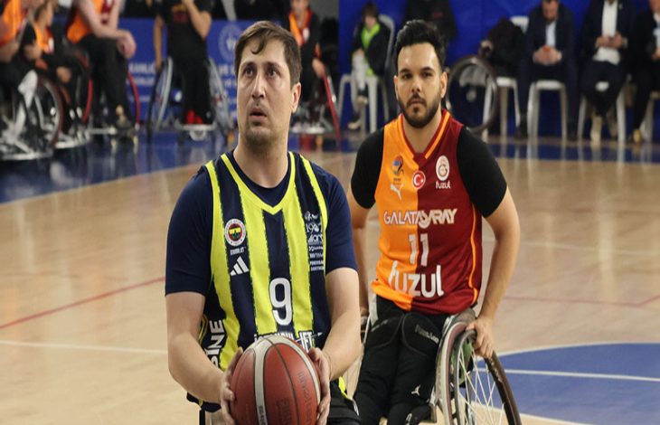 Bir spor salonunda tekerlekli sandalyede basketbol oynayan iki sporcu görülüyor. Önde topu elinde tutan sporcu şuta hazırlanırken, arkasındaki rakip oyuncu savunmada; maçın ciddiyeti ve rekabet duygusu öne çıkıyor.