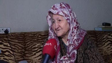 Evinde röportaj veren yaşlı bir kadın, başörtüsüyle koltukta otururken DHA mikrofonuna konuşuyor; yüzündeki ifade yaşadığı zorluğu ve yardım beklentisini yansıtıyor.