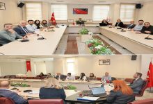 İki kareden oluşan görüntüde üniversite toplantı salonunda uzun masalar etrafında toplanmış bir kurul görülüyor. Türk bayrakları, mikrofonlar ve dizüstü bilgisayarlar eşliğinde resmi bir görüşme sürüyor; odada “erişilebilirlik için kafa yorulan” ciddi ama umutlu bir atmosfer var.