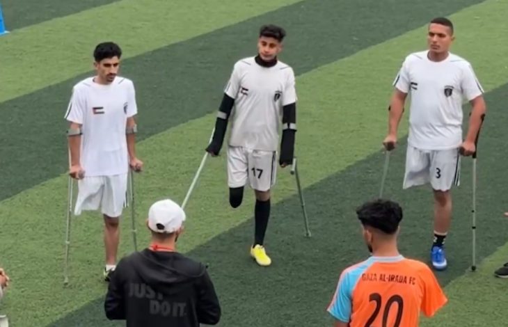 Beyaz formalı üç ampute futbolcu sahaga, karşılarında hocaları ve turuncu formalı sporcu bulunuyor.