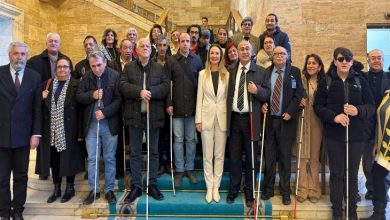 Merdivenlerde toplu fotoğraf veren kalabalık bir grup, çoğu beyaz baston taşıyan görme engelli bireylerden oluşuyor; ortada takım elbiseli kişilerle birlikte dayanışma ve görünürlük mesajı öne çıkıyor.