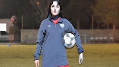 Hümeyra Alantaş, spor kıyafetiyle futbol sahasında ayakta dururken, sol protez kolunun altında topu tutarak poz veriyor.