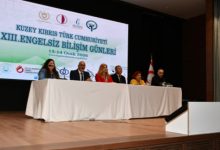 Bir konferans salonunda sahneye kurulmuş uzun masada oturan konuşmacılar, “Engelsiz Bilişim Günleri” başlıklı etkinlik kapsamında panel gerçekleştiriyor; arkadaki büyük ekranda etkinliğin adı ve logolar yer alıyor.