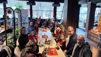 Uzun bir masanın etrafında babalar ve çocuklar birlikte oturuyor. Masada içecekler ve atıştırmalıklar var. Çocukların ellerinde kırmızı bayraklar dikkat çekiyor. Arka planda LÖSEV logosu görülüyor; mekân sıcak, kalabalık ve ailece geçirilen neşeli bir gün hissi veriyor.