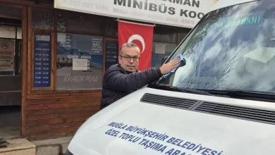 Minibüs durağı önünde bir şoför, belediyeye ait toplu taşıma aracının ön camını siliyor. Arkada Dalaman Minibüs Kooperatifi tabelası ve Türk bayrağı görünüyor.