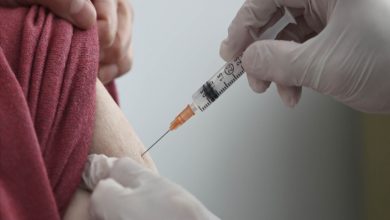 Beyaz eldivenli bir sağlık çalışanının, bir kişinin koluna enjektörle aşı yaptığı anı gösteren yakın çekim bir görseldir.