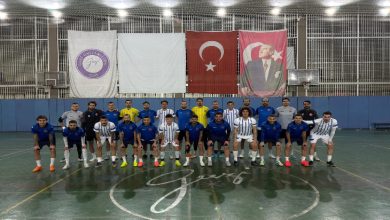 Kapalı bir spor salonunda, Türkiye İşitme Engelliler Futsal Milli Takımı toplu halde kamera karşısında dizilmiş. Mavi ve beyaz formalarla iki sıra halinde poz veriyorlar. Arkada Türk bayrağı ve Atatürk posteri asılı; salon ışıkları parlak ve düzenli.