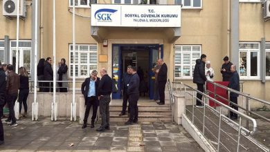 Bir kamu binasının önünde, SGK İl Müdürlüğü girişinde bekleyen ve sohbet eden kalabalık bir grup; rampalı giriş, merdivenler ve bina tabelası net şekilde görülüyor.