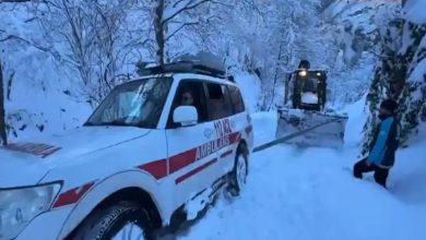 Yoğun karla kaplı bir yolda, kar küreme aracının açtığı güzergahta ilerleyen bir ambulans görülüyor; çevre bembeyaz, ekipler zorlu kış koşullarında müdahale halinde.