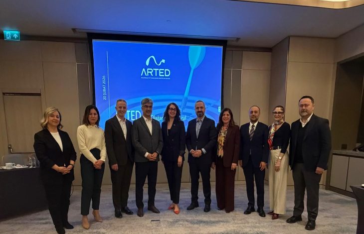 Görselde, bir toplantı salonunda yan yana dizilmiş şekilde poz veren dokuz kişilik bir grup görülüyor. Arkada büyük ekranda ARTED logosu ve toplantıya ait sunum yansıtılmış. Kişiler resmi kıyafetleriyle, toplantı veya genel kurul etkinliği sonrasında hatıra fotoğrafı çektiriyor gibi görünüyor.