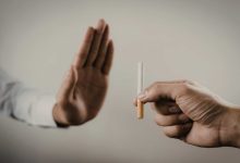 Sade bir arka plan önünde iki el görünüyor. Sağ taraftaki el bir sigara tutarken, sol taraftaki el avuç içi dışa dönük şekilde “dur” işareti yapıyor. Görsel, sigaraya karşı mesafe koymayı ve bırakma mesajını simgeliyor.