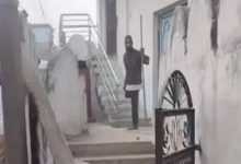 Dar ve taş bir geçitte, merdivenlerin bulunduğu eski bir yapı görülüyor. Merdiven başında elinde sopa benzeri bir nesne tutan bir kişi ayakta duruyor; çevrede duvarlar, metal korkuluklar ve giriş kapıları yer alıyor.