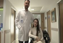 Ortopedi ve Travmatoloji Uzmanı Doç. Dr. Bilgehan Çatal ayakta dururken, hastası Lejla Gusinjac tekerlekli sandalyede oturuyor ve hastane koridorunda poz veriyor.