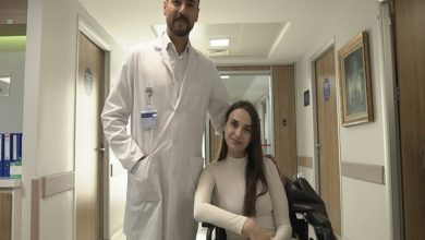 Ortopedi ve Travmatoloji Uzmanı Doç. Dr. Bilgehan Çatal ayakta dururken, hastası Lejla Gusinjac tekerlekli sandalyede oturuyor ve hastane koridorunda poz veriyor.