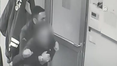 Bir güvenlik kamerası görüntüsünde, kapı önünde duran bir görevlinin öksüren bir kişiye arkadan sarılarak müdahalede bulunduğu görülüyor. Ortam kapalı bir alan; kişi boğulma anında yardım alıyor.